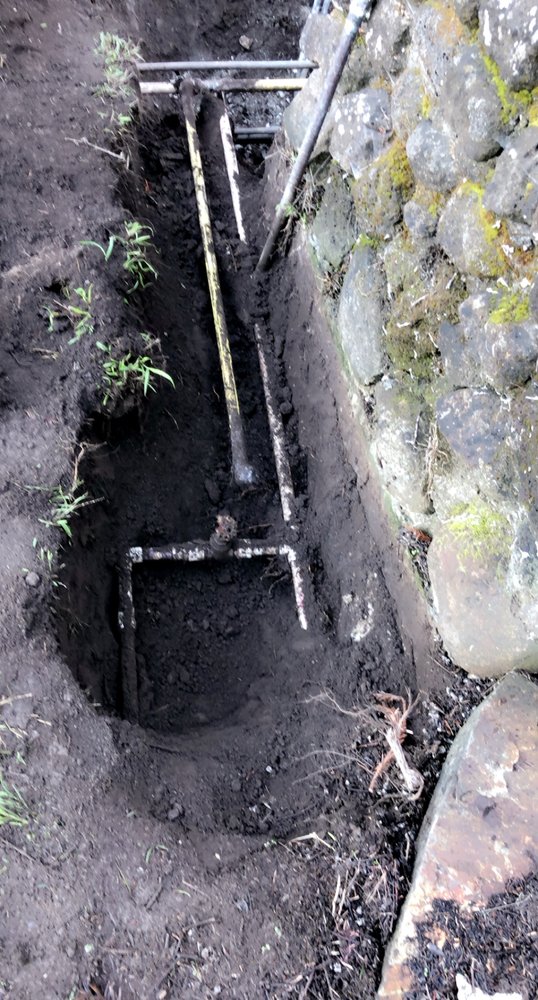 Irrigation trench dug alongside a stone wall with pipes installed